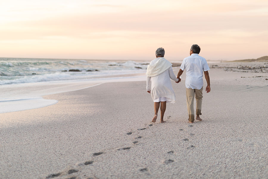 Multiracial senior couple holding hands walking together while leaving footprints on sand