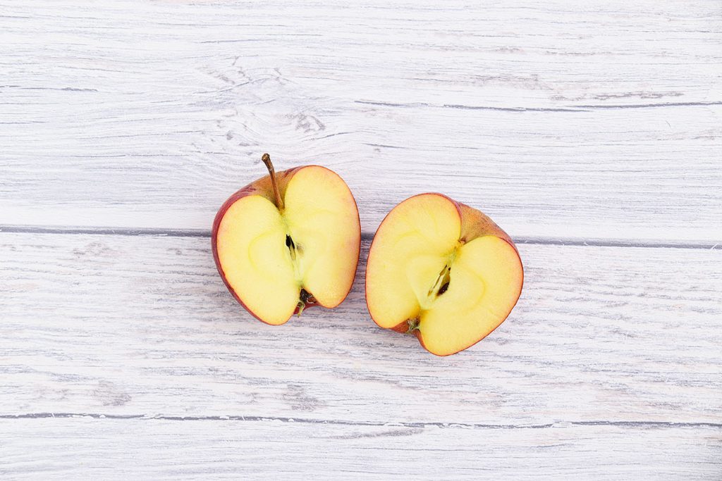 Apple cut in half on white wooden background